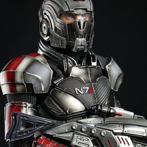 以下が含まれることがあります： バイザー付きのヘルメットをかぶり、銃を持った未来的な兵士の黒と赤のフィギュア。兵士の胸の鎧には「N7」の文字が印刷されています。