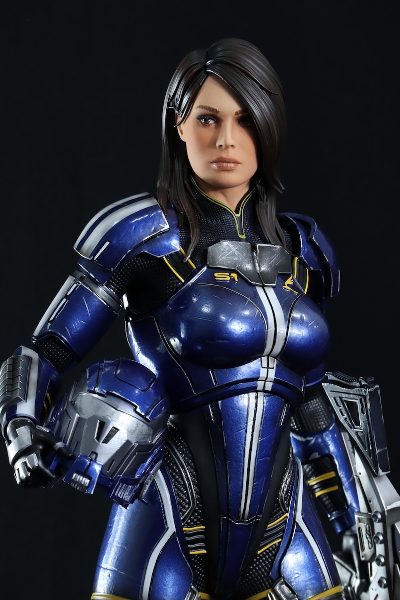 May include: A female action figure wearing a blue and silver spacesuit with a black and yellow design. The figure has long dark hair and is holding a helmet in her left hand.