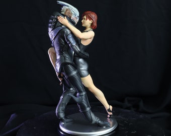 Könnte beinhalten: Eine schwarze und silberne Figur eines tanzenden Paares. Die männliche Figur trägt einen schwarzen Anzug mit silbernen Akzenten und hat einen silbernen Kopf. Die weibliche Figur trägt ein schwarzes Kleid und hat rote Haare.