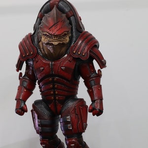 May include: A red and black action figure of a fictional alien warrior wearing armor. The figure has a detailed sculpt and paint job.