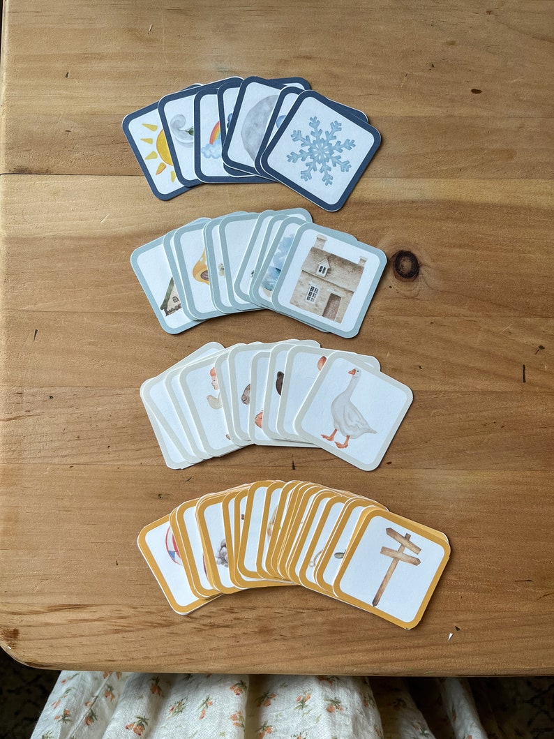 May include: A set of 48 illustrated cards featuring various images, including a sun, a rainbow, a snowflake, a house, a goose, and a signpost. The cards are divided into four groups, each with a different colour border: blue, green, white, and yellow.