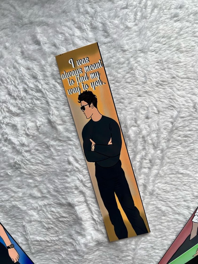 May include: A bookmark with an illustration of a man in sunglasses, black shirt, and trousers. The bookmark has the text "I was always meant to find my way to you" in white font. The background is a gradient of gold and orange.