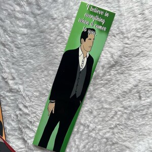 May include: A green bookmark with an illustration of a man in a black suit and the text "I believe in everything when it comes to you." The bookmark has a white background and a green border.