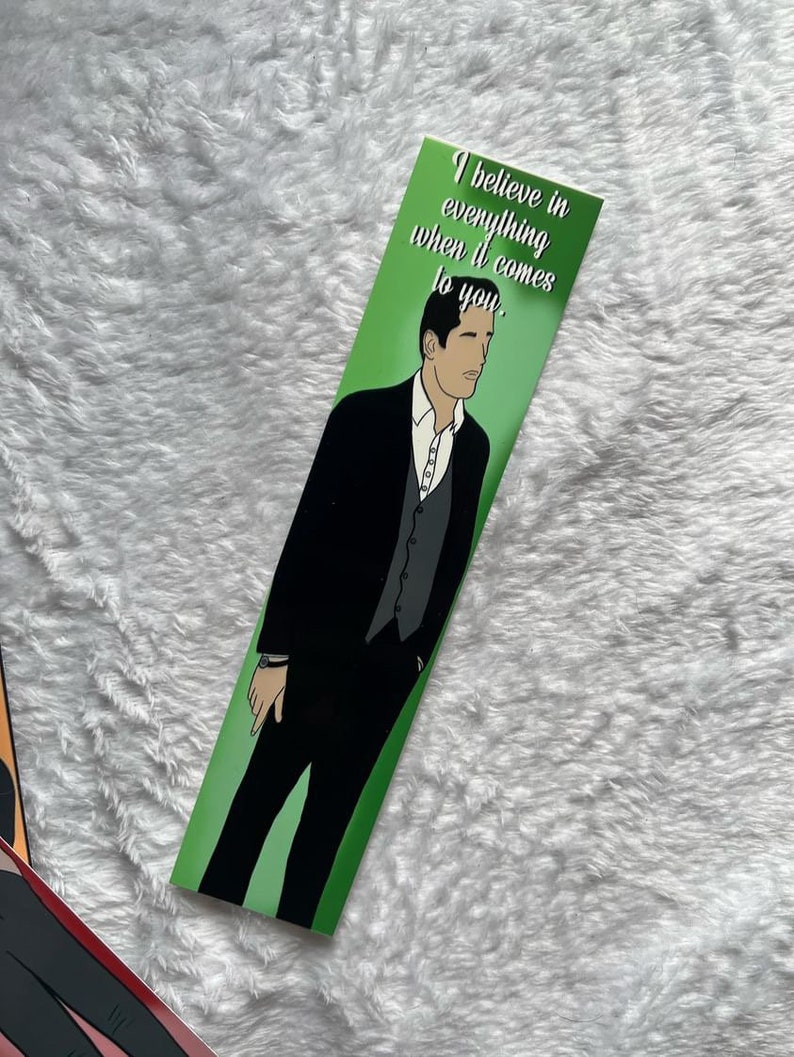 May include: A green bookmark with an illustration of a man in a black suit and the text "I believe in everything when it comes to you." The bookmark has a white background and a green border.