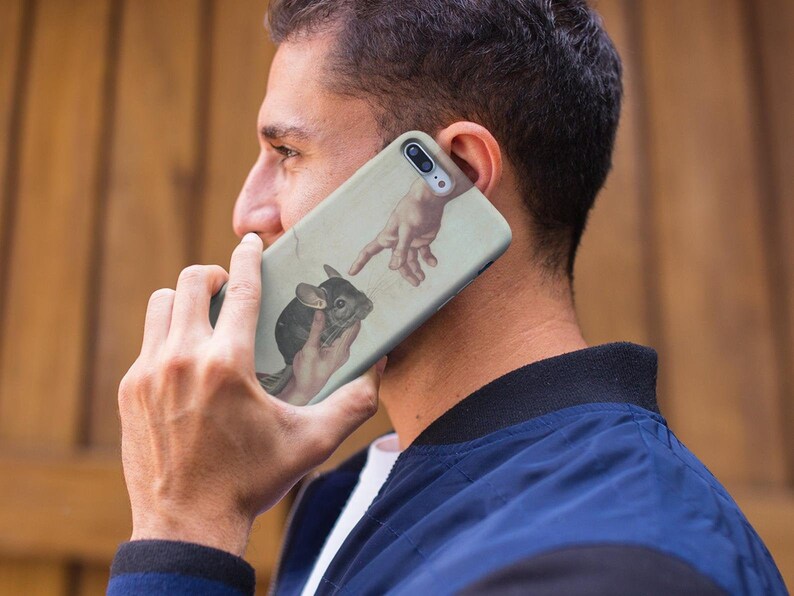 May include: A phone case with a chinchilla illustration, inspired by Michelangelo's The Creation of Adam. The design shows a chinchilla held in a hand, with another hand reaching towards it. The case has a light beige background.
