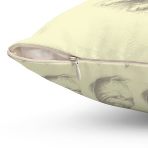 May include: A decorative pillow with a light yellow background and a repeating pattern of sketched faces. The pillow has a zipper closure and a neutral-colored zipper pull.