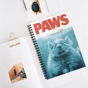 May include: A spiral bound notebook with a Jaws-inspired design featuring a chinchilla in the water with the text "PAWS" in red letters.