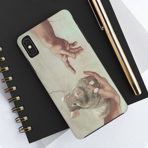 May include: A phone case featuring a parody of Michelangelo's 'The Creation of Adam,' with a chinchilla replacing Adam. The design depicts two hands reaching towards each other, with the chinchilla in one hand. The case has a light beige background.