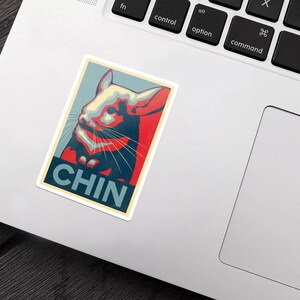 Peut inclure: Une affiche rouge, blanche et bleue avec un chinchilla de dessin anim&eacute;. L'affiche dit "CHIN" en lettres blanches en gras.