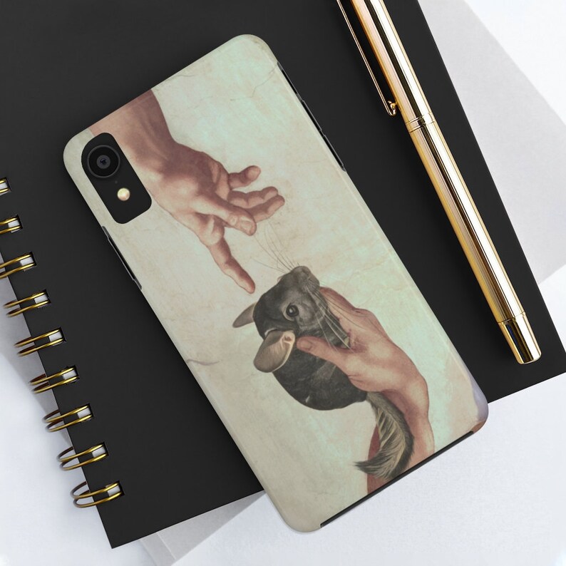 May include: A phone case with a humorous design based on Michelangelo's 'The Creation of Adam,' replacing Adam with a chinchilla. The case has a beige and white background. The phone case is on a black notebook.