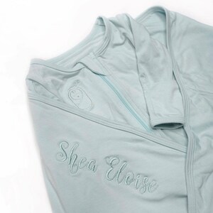 May include: A light blue baby swaddle with a zipper closure and the name "Shea Eloise" embroidered on the front.