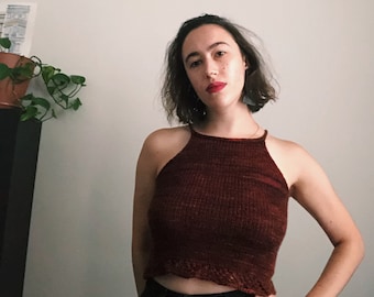 May include: A woman wearing a maroon knit halter top with a crocheted trim and black jeans.