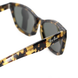 May include: Tortoise shell Ray-Ban sunglasses with green lenses. The sunglasses have a classic, angular shape and a subtle tortoise shell pattern.