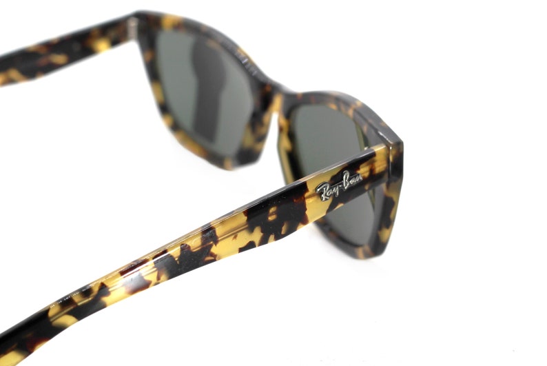 May include: Tortoise shell Ray-Ban sunglasses with green lenses. The sunglasses have a classic, angular shape and a subtle tortoise shell pattern.