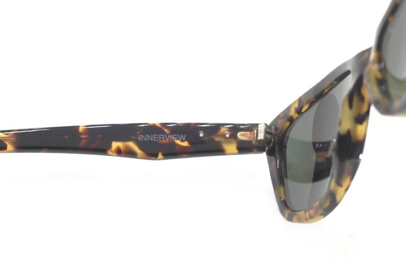 May include: Tortoise shell sunglasses with dark green lenses. The sunglasses have the word "INNERVIEW" printed on the frame.