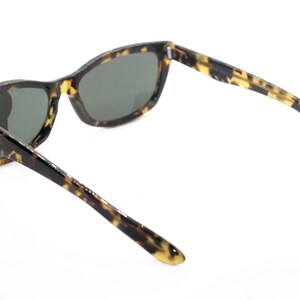 May include: Tortoiseshell sunglasses with dark lenses. The sunglasses have a classic, rectangular shape with a slightly curved frame.