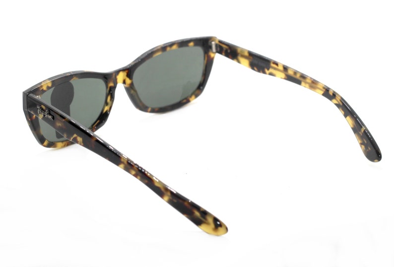 May include: Tortoiseshell sunglasses with dark lenses. The sunglasses have a classic, rectangular shape with a slightly curved frame.