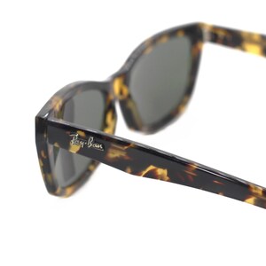 May include: Tortoise shell Ray-Ban sunglasses with dark green lenses. The sunglasses have a sharp, angular shape.