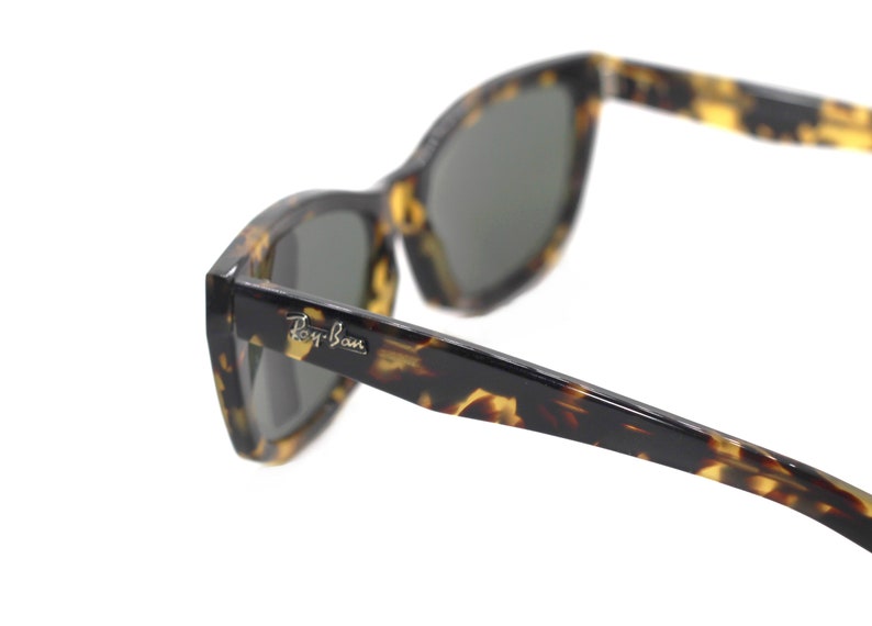 May include: Tortoise shell Ray-Ban sunglasses with dark green lenses. The sunglasses have a sharp, angular shape.