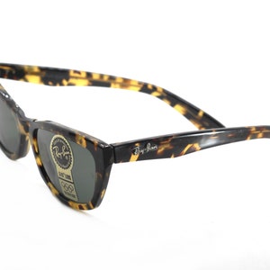 May include: Tortoise shell Ray-Ban sunglasses with green lenses. The sunglasses have a classic, rectangular shape and a thin frame.