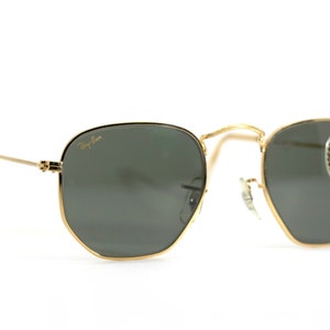 Może przedstawiać: Okulary przeciwsłoneczne w złotej oprawie z zielonymi szkłami. Okulary mają logo Ray-Ban na lewej szklance i naklejkę na prawej szklance z napisem "Ray-Ban G-15 LENS".