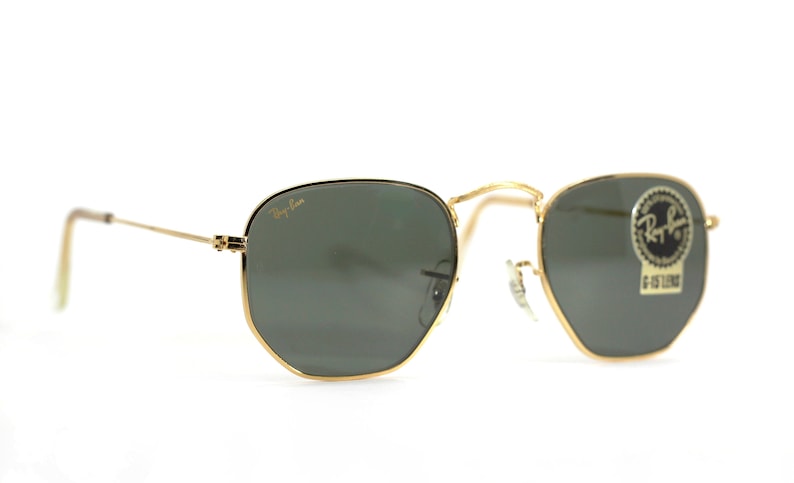 Może przedstawiać: Okulary przeciwsłoneczne w złotej oprawie z zielonymi szkłami. Okulary mają logo Ray-Ban na lewej szklance i naklejkę na prawej szklance z napisem "Ray-Ban G-15 LENS".
