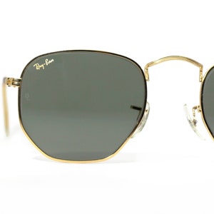 Może przedstawiać: Okulary przeciwsłoneczne w złotej oprawie z ciemnozielonymi szkłami. Okulary mają logo Ray-Ban na prawym szkle.