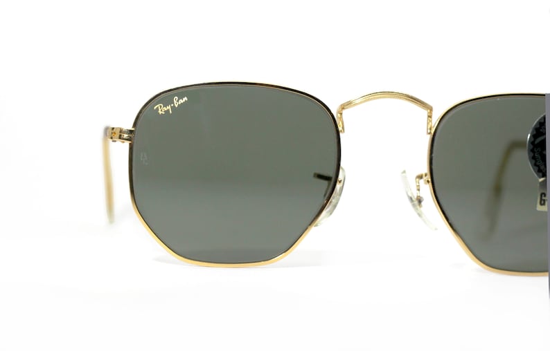 Może przedstawiać: Okulary przeciwsłoneczne w złotej oprawie z ciemnozielonymi szkłami. Okulary mają logo Ray-Ban na prawym szkle.