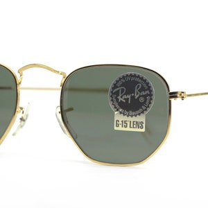 Może przedstawiać: Okulary przeciwsłoneczne w złotej oprawie z zielonymi szkłami. Okulary mają naklejkę Ray-Ban na prawym szkle, na kt&oacute;rej widnieje napis "100% UV protection Ray-Ban Series by Bausch & Lomb G-15 Lens".