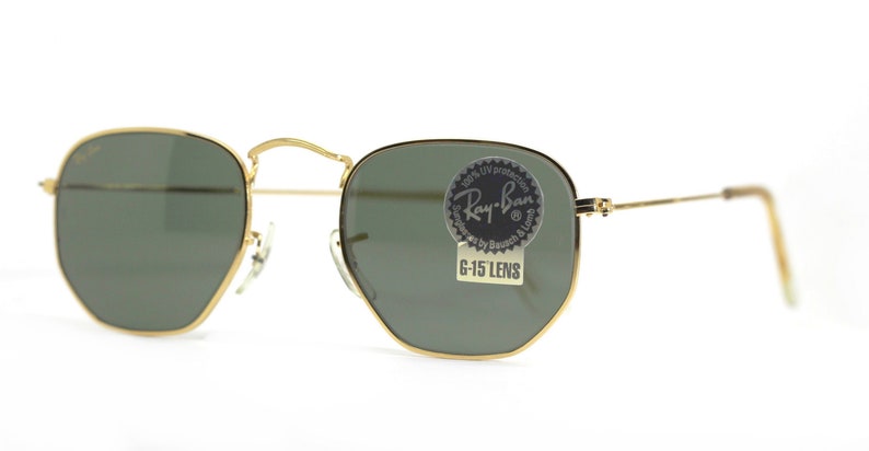 Może przedstawiać: Okulary przeciwsłoneczne w złotej oprawie z zielonymi szkłami. Okulary mają naklejkę Ray-Ban na prawym szkle, na kt&oacute;rej widnieje napis "100% UV protection Ray-Ban Series by Bausch & Lomb G-15 Lens".