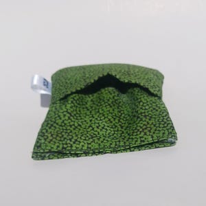 May include: A small green fabric pouch with a white tag. The pouch has a black and green speckled pattern.