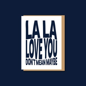 May include: White card with black text that reads "LA LA LOVE YOU DON'T MEAN MAYBE"