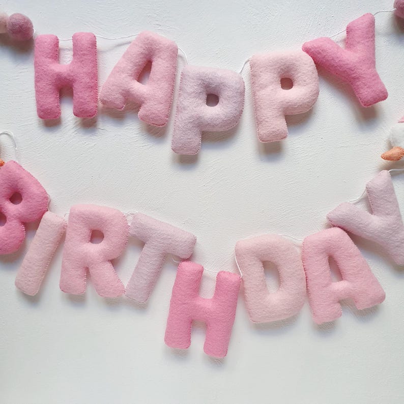 May include: Pink felt banner with the words "Happy Birthday" strung together with white thread.