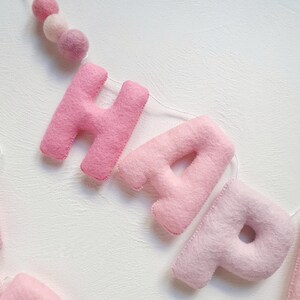 May include: Pink felt letter banner spelling out "Happy" with a string of pink felt balls.