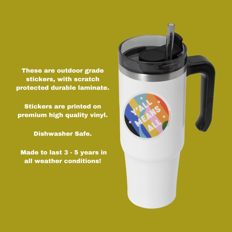 May include: White travel mug with a black handle and lid. The mug has a colorful sticker that says "Y'all Means All".