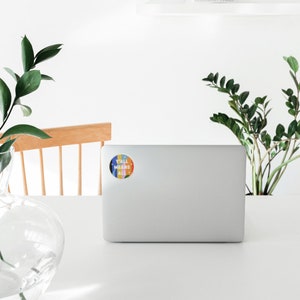 May include: A white laptop computer with a colorful round sticker that says "Y'all Means All" on the back.