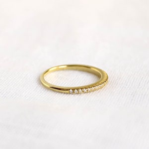 An elegant 18k gold plated half eternity band with pavé cubic zirconia stones delicately set around the band. This ring is a perfect matching wedding band, with its dainty design and timeless beauty.