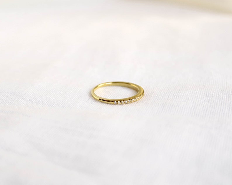 An elegant 18k gold plated half eternity band with pavé cubic zirconia stones delicately set around the band. This ring is a perfect matching wedding band, with its dainty design and timeless beauty.