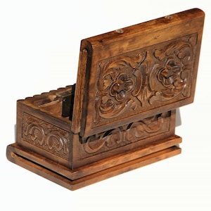 May include: A wooden box with intricate carvings on the lid and sides. The lid is open, revealing the empty interior of the box.