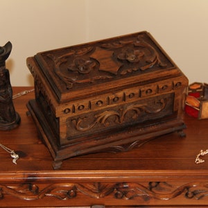 Può includere: Una scatola di legno con intagli intricati, una statuetta di legno e due collane su un tavolo di legno.