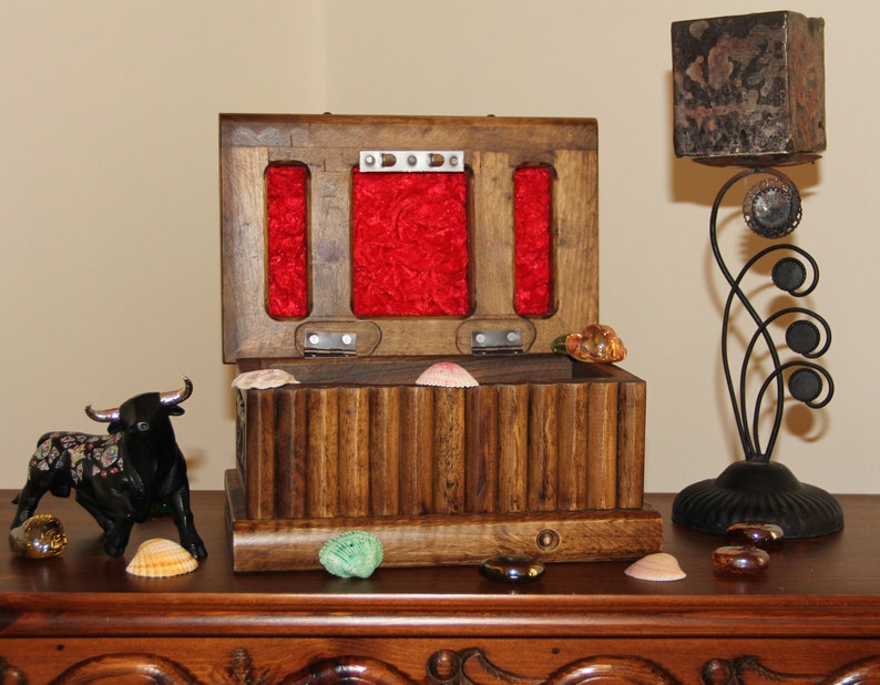May include: A wooden box with a red velvet interior and a hinged lid. The box is open and has a series of small compartments inside. The box is sitting on a wooden table with a black bull figurine and seashells.