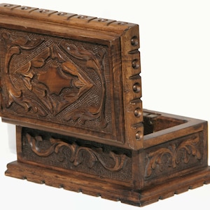 May include: A wooden box with an open lid, showcasing intricate carved floral and geometric patterns. The box is a rich brown color, with detailed carvings on the lid and sides. The lid is slightly ajar, revealing the interior.