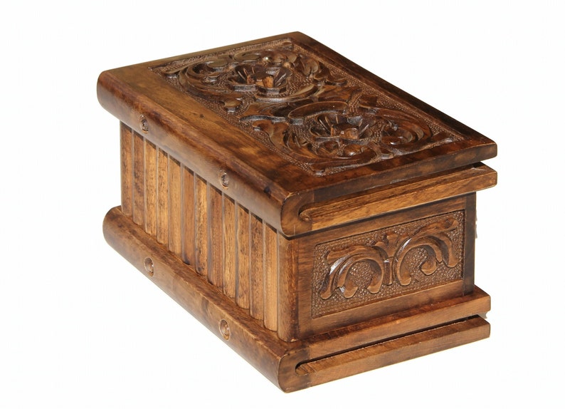 May include: A wooden box with intricate carvings on the top and sides. The box is made of dark brown wood and has a hinged lid.