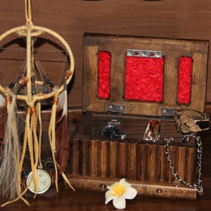May include: A wooden jewelry box with a hinged lid, featuring a red velvet interior and multiple compartments. The box is open, revealing a watch, bracelets, and a chain necklace. A dreamcatcher with feathers hangs in the background.