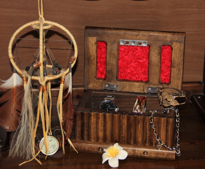 May include: A wooden jewelry box with a hinged lid, featuring a red velvet interior and multiple compartments. The box is open, revealing a watch, bracelets, and a chain necklace. A dreamcatcher with feathers hangs in the background.