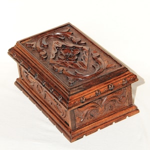 May include: A dark brown wooden box with intricate carvings of floral designs. The box has a hinged lid and is made of solid wood.