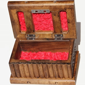 May include: A wooden box with a hinged lid and a red velvet interior. The box has a carved design on the front and sides.