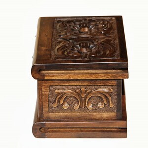 May include: A wooden box with intricate carvings on the top and front. The box is closed and has a dark brown finish.