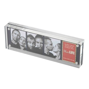 May include: A clear acrylic photo frame with a black backing and silver magnetic closures. The frame holds a photo strip with five images of people making funny faces. The frame has a red and white label that says "Another Great Photo-Strip Product from PhotoLIFE photo-life.com.au".