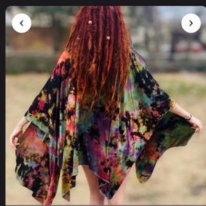 May include: A loose-fitting poncho featuring a vibrant tie-dye pattern with blended colors of black, pink, yellow, and teal. The garment has an asymmetrical hemline and wide, flowing sleeves that drape over the arms, creating a relaxed silhouette.
